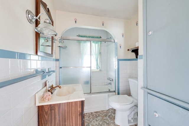 full bath with tile walls, tile patterned floors, vanity, bath / shower combo with glass door, and toilet