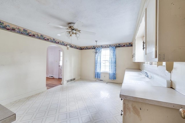 kitchen featuring light flooring, a sink, arched walkways, ceiling fan, and light countertops