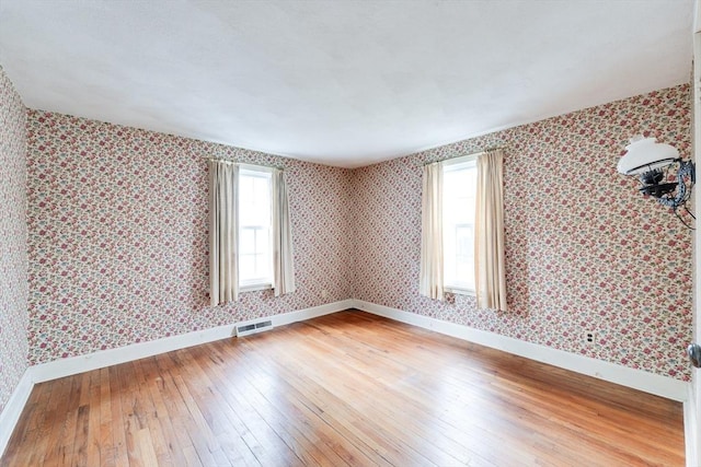 spare room featuring healthy amount of natural light, light wood finished floors, baseboards, and wallpapered walls