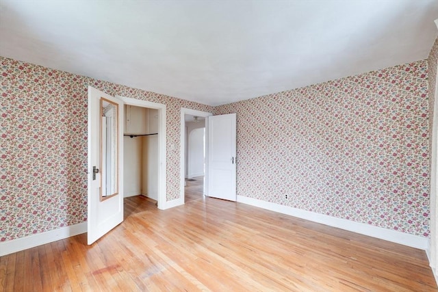 unfurnished bedroom with wallpapered walls, light wood-style floors, baseboards, and a closet