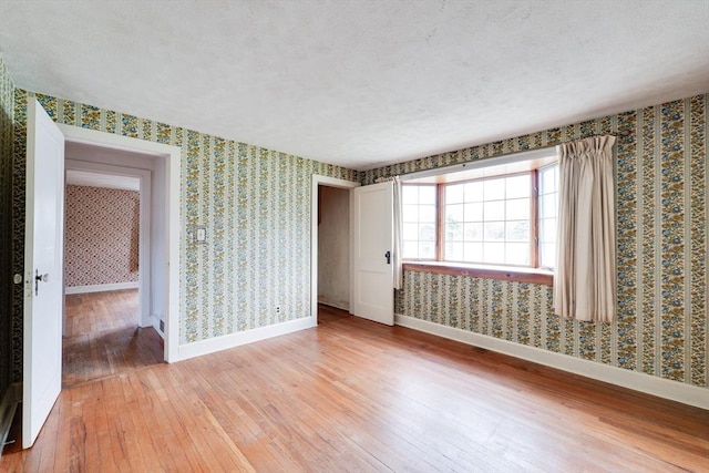 unfurnished room featuring light wood-style flooring, wallpapered walls, and baseboards