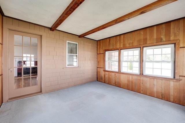 carpeted spare room featuring wood walls and beamed ceiling