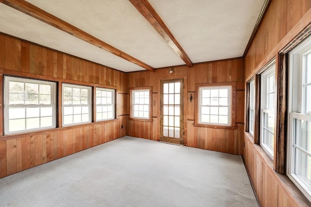 empty room with wood walls, light carpet, and beam ceiling