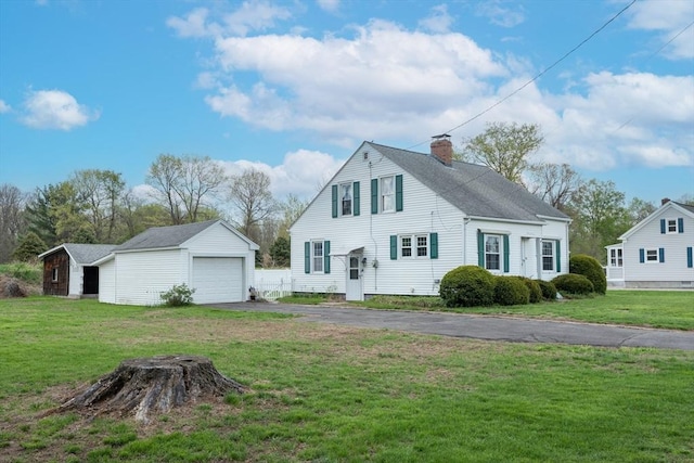 view of front of house with an outbuilding, a chimney, asphalt driveway, a detached garage, and a front lawn