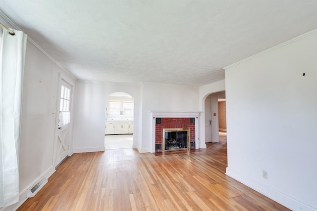 unfurnished living room featuring arched walkways, light wood-style floors, a brick fireplace, and baseboards
