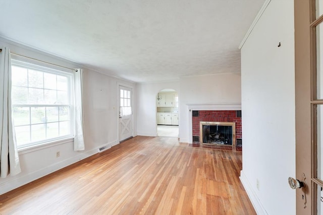 unfurnished living room with arched walkways, light wood finished floors, baseboards, and a fireplace