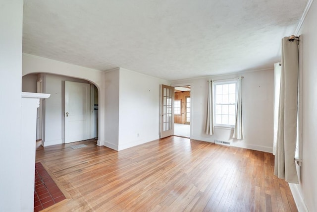 unfurnished living room with arched walkways, light wood-style floors, baseboards, and ornamental molding