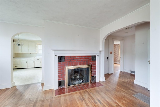 unfurnished living room with light wood-type flooring, a brick fireplace, baseboards, and crown molding