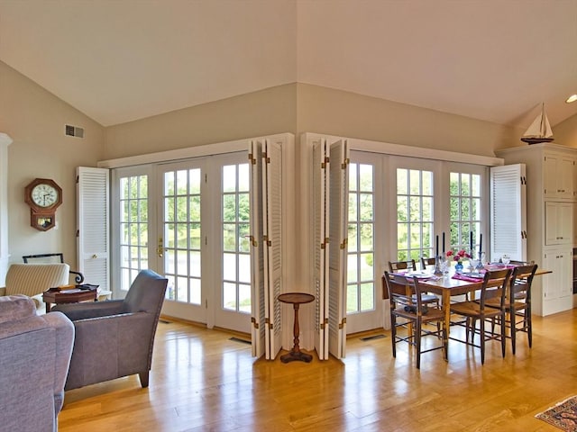 dining space featuring french doors, light hardwood / wood-style floors, plenty of natural light, and high vaulted ceiling