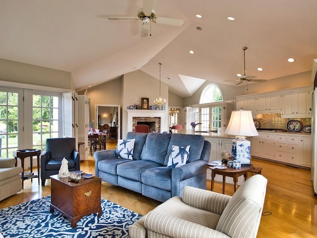 living room with ceiling fan with notable chandelier, light hardwood / wood-style flooring, and vaulted ceiling