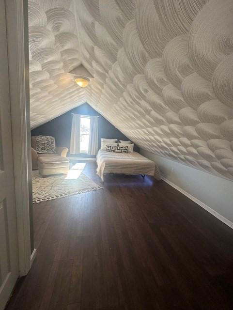 unfurnished bedroom featuring baseboards, lofted ceiling, and wood finished floors