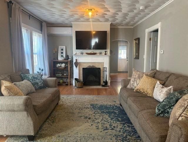 living room with arched walkways, a tile fireplace, crown molding, and wood finished floors