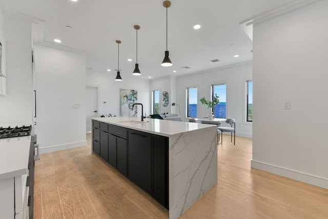 kitchen featuring a large island, sink, stainless steel gas range, light hardwood / wood-style flooring, and decorative light fixtures