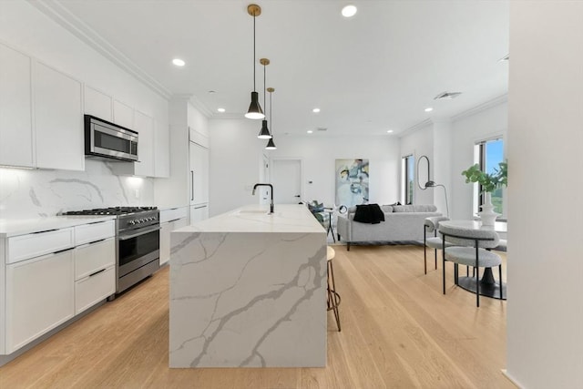 kitchen featuring white cabinets, decorative light fixtures, stainless steel appliances, and an island with sink