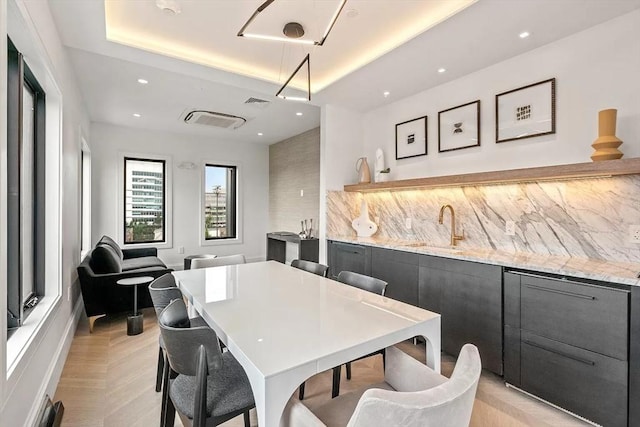 dining space featuring light parquet floors, sink, and a tray ceiling