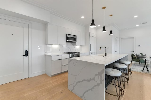 kitchen featuring backsplash, a kitchen island with sink, sink, white cabinetry, and hanging light fixtures