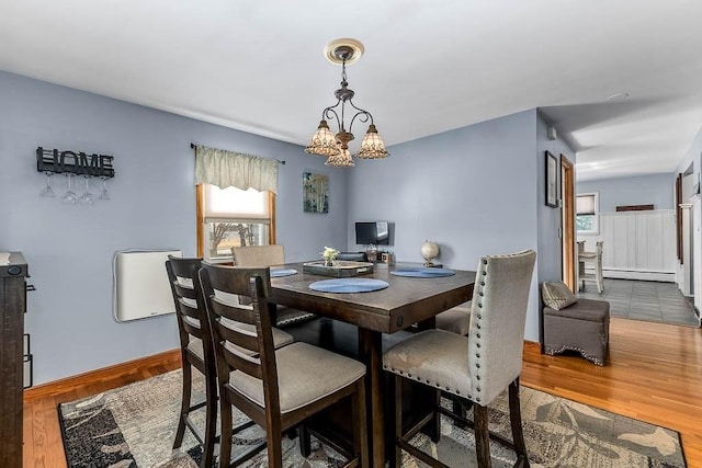 dining area featuring baseboards, a notable chandelier, a baseboard heating unit, and wood finished floors