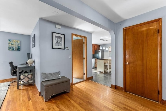 living area with arched walkways, light wood-style flooring, and baseboards