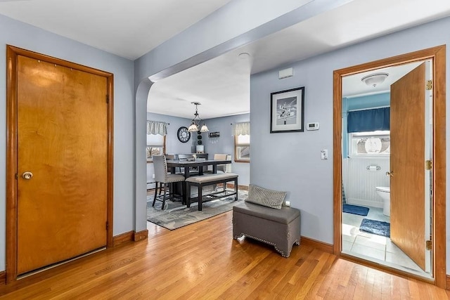 corridor with arched walkways, a notable chandelier, light wood-style flooring, and baseboards