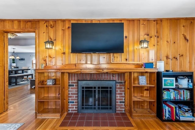 living room featuring wood walls, a brick fireplace, wood finished floors, and an inviting chandelier