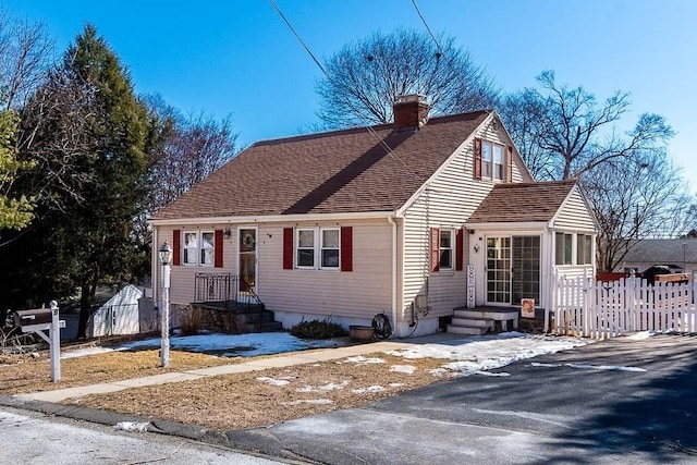 view of front facade featuring a shingled roof, a chimney, and fence