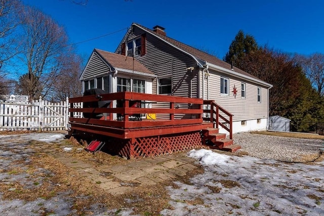 snow covered property featuring a deck, a shingled roof, fence, a gate, and a chimney