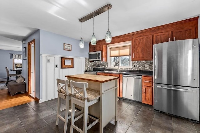 kitchen featuring tasteful backsplash, wooden counters, appliances with stainless steel finishes, a kitchen island, and a kitchen bar