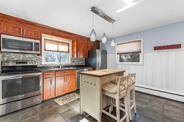 kitchen with a wainscoted wall, butcher block counters, a breakfast bar area, appliances with stainless steel finishes, and a sink