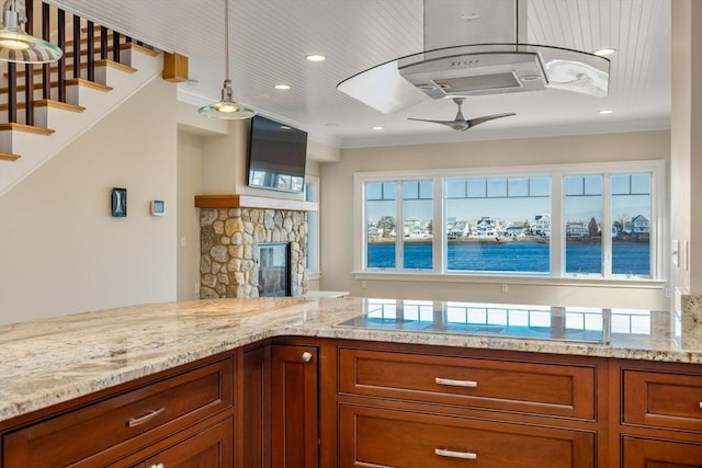 kitchen featuring ceiling fan, brown cabinets, hanging light fixtures, light stone countertops, and a fireplace