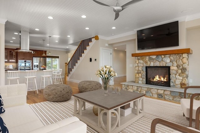 living room featuring light wood-style flooring, a fireplace, baseboards, stairs, and ornamental molding