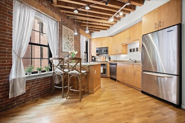 kitchen with light brown cabinets, brick wall, a kitchen breakfast bar, light countertops, and appliances with stainless steel finishes