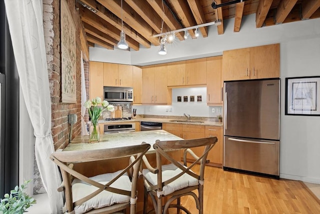 kitchen with stainless steel appliances, a peninsula, a sink, light countertops, and light brown cabinetry