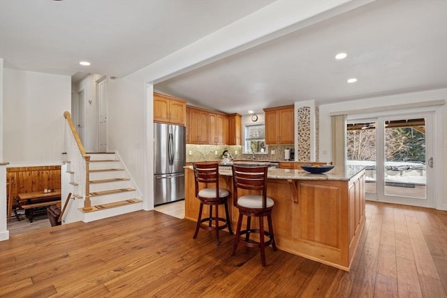 113 Glen Rd, Gorham, NH 03581 - kitchen with freestanding refrigerator, light wood-style flooring, backsplash, light stone counters, and a kitchen bar