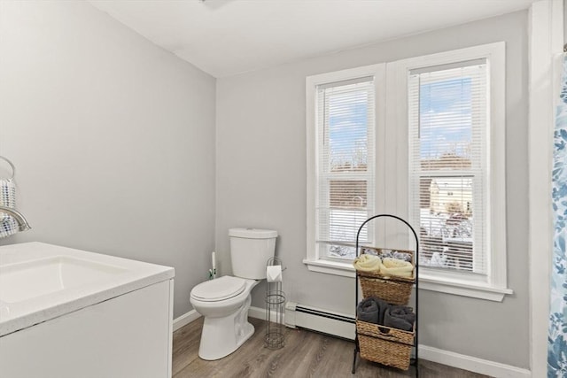 bathroom featuring wood-type flooring, a baseboard heating unit, toilet, and a healthy amount of sunlight