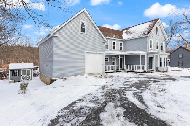 snow covered property featuring a porch and a storage unit