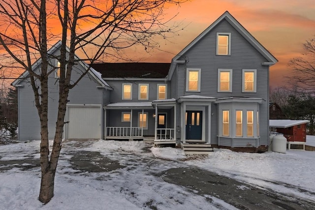 snow covered property featuring covered porch and a garage