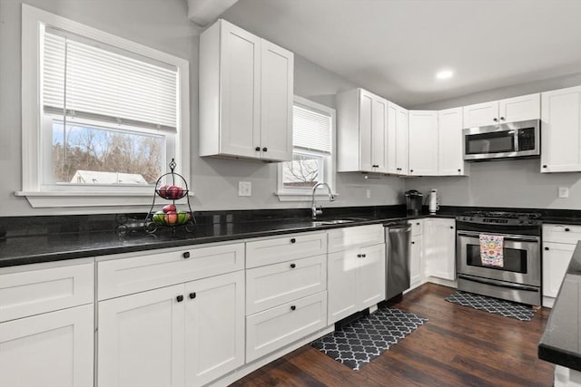 kitchen featuring white cabinets, appliances with stainless steel finishes, dark hardwood / wood-style flooring, and dark stone counters