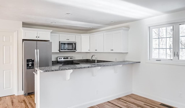 kitchen with white cabinets, kitchen peninsula, appliances with stainless steel finishes, and a kitchen breakfast bar