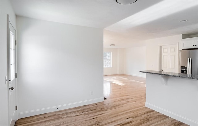 interior space with stainless steel fridge with ice dispenser, dark stone counters, white cabinets, and light hardwood / wood-style floors