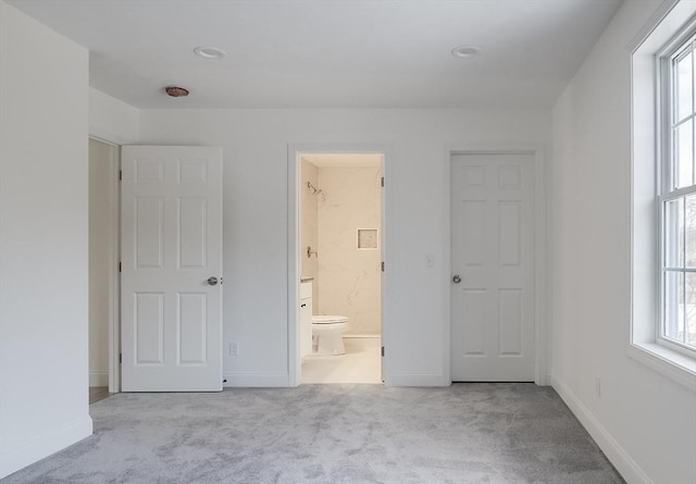 unfurnished bedroom featuring multiple windows, light colored carpet, and ensuite bath