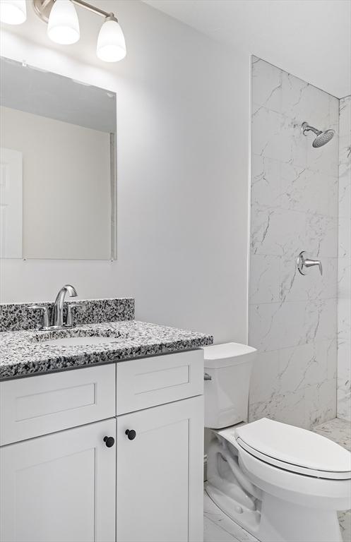 bathroom with tiled shower, toilet, and vanity