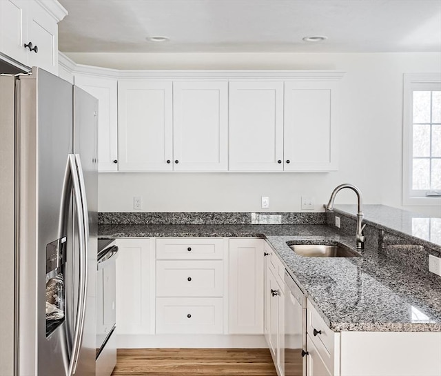 kitchen featuring appliances with stainless steel finishes, sink, dark stone countertops, white cabinets, and light hardwood / wood-style flooring