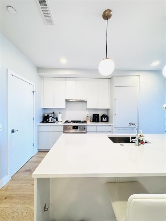 kitchen with stainless steel range, a sink, light wood-style flooring, decorative backsplash, and visible vents