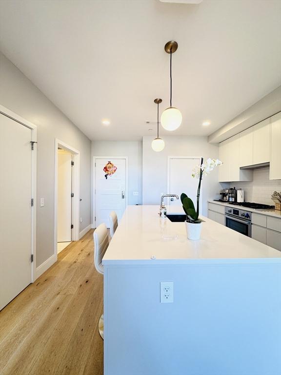 kitchen featuring oven, light wood-style floors, light countertops, white cabinetry, and a sink