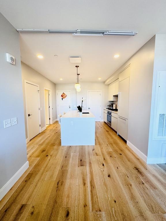 kitchen with baseboards, white cabinets, light wood-style flooring, and range