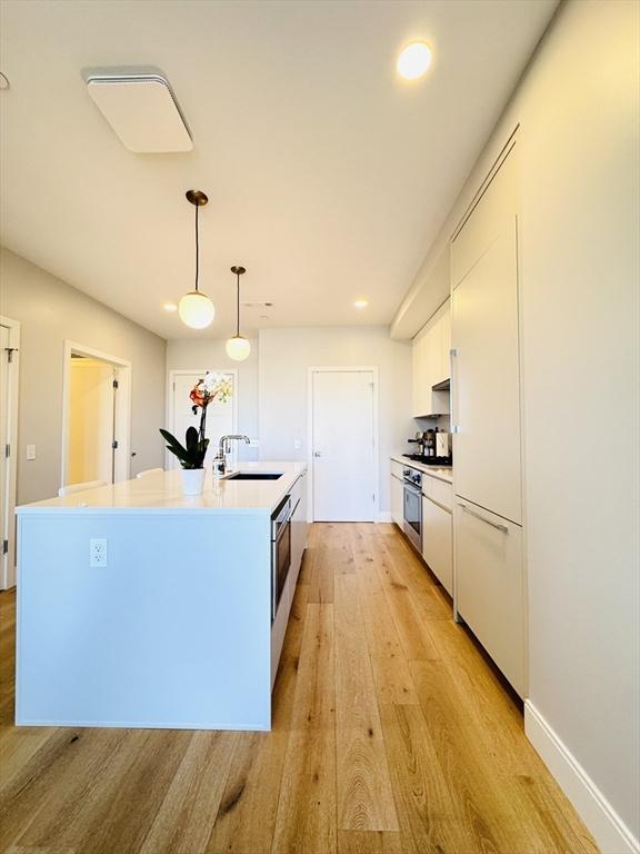 kitchen with white cabinets, a sink, light countertops, stainless steel oven, and light wood-style flooring