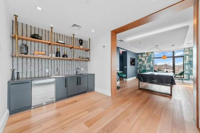 bar with visible vents, baseboards, indoor wet bar, a sink, and light wood finished floors
