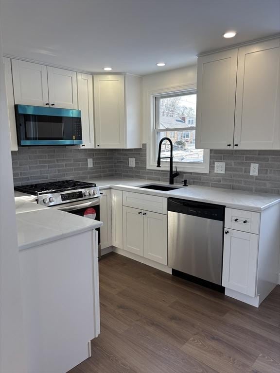 kitchen with dark wood-type flooring, sink, appliances with stainless steel finishes, white cabinets, and backsplash