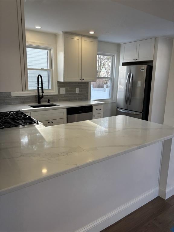 kitchen featuring appliances with stainless steel finishes, sink, white cabinets, light stone counters, and dark wood-type flooring