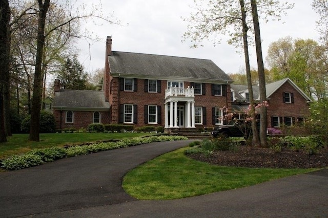 colonial inspired home featuring a balcony and a front lawn